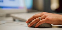 Hand auf Computermouse, im Hintergrund Tastatur und Bildschirm