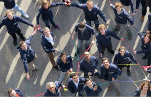 Eine Gruppe von Menschen bildet mit Hilfe bunter Bänder ein Netz.