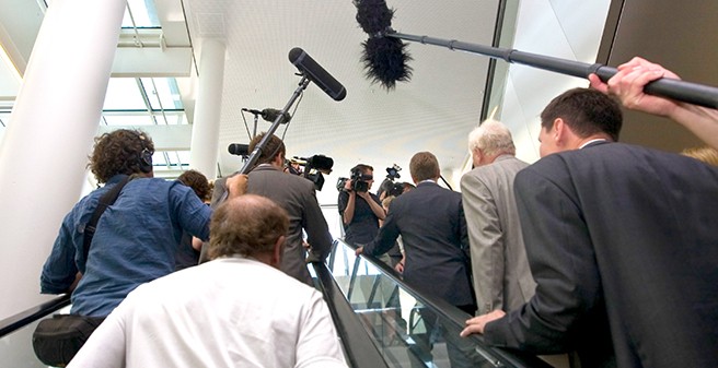Journalisten mit Fernsehkameras und Mikrofonen fahren eine Rolltreppe hoch