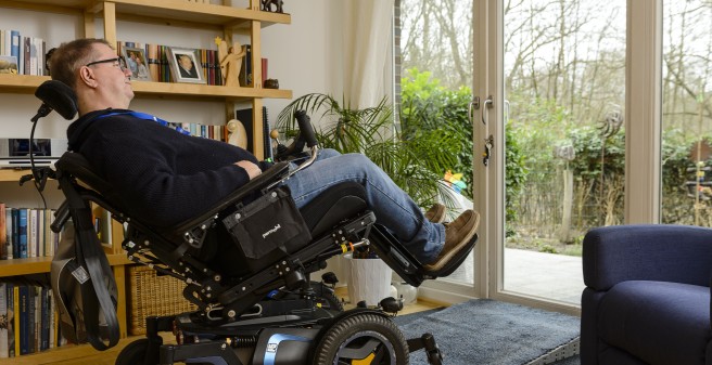 Tomas Gerlach in seinem Wohnzimmer. Er entspannt, halb liegend, im Rollstuhl und schaut in den Garten