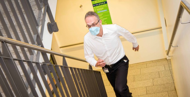 Sven Gerber läuft eine Treppe hinauf. Er trägt eine hellblaue Atemschutzmaske