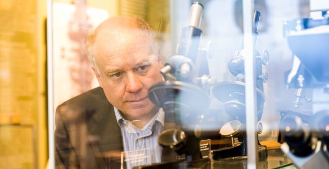 Prof Osten blickt in einen Schaukasten mit historischen Mikroskopen
