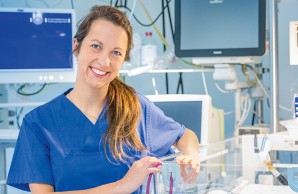Dr. Theresa Harbauer lehnt am Wärme-Bett eines Neugeborenen und lächelt mit leicht geneigtem Kopf in die Kamera