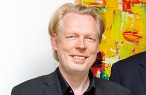   Prof. Dr. Jürgen Gallinat lächelt in die Kamera. Gallinat ist hellblond, er trägt ein schwarzes Hemd und Jacket