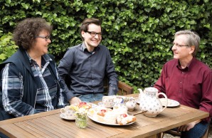 lachend sitzt Simon Arndt mit seinen Eltern am Kaffeetisch