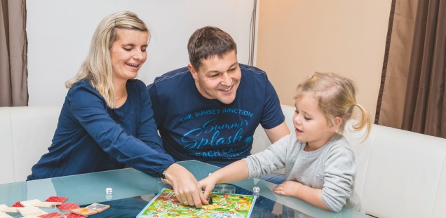 Sandra Fink, Mann Ronny und Tochter Anni spielen ein Brettspiel am Wohnzimmertisch