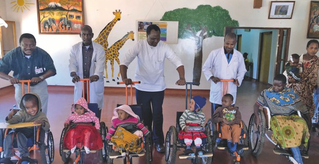 Ärzte stehen mit Kindern im Rollstuhl in einem mit afrikanischen Motiven bemaltem Raum