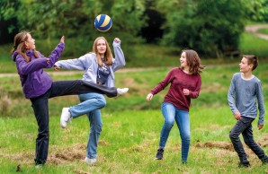 Vier Jugendliche spielen mit einem Ball, zwei verrenken sich, um den in der Luft fliegenden Ball mit dem Fuß zu treffen.