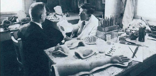 Der Mouleur Ary Bergen mit Pinsel und Palette beim Bemalen eines Patienten, der von hinten zu sehen ist