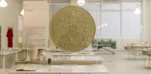 vergrößerte Replik einer goldenen Münze mit lateinischer Inschrift, aufgehängt über den Ausstellungstischen