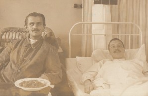 Zwei Verwundete in Krankenbetten, einer Hälte einen Teller mit Suppe